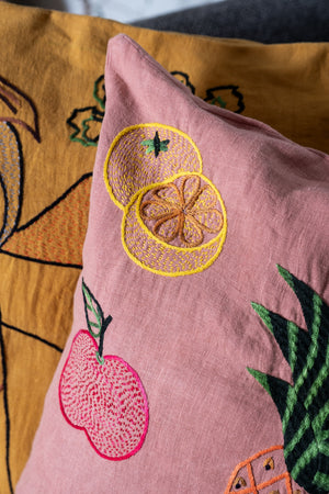 Pink pillow with embroidered fruit design on a yellow background