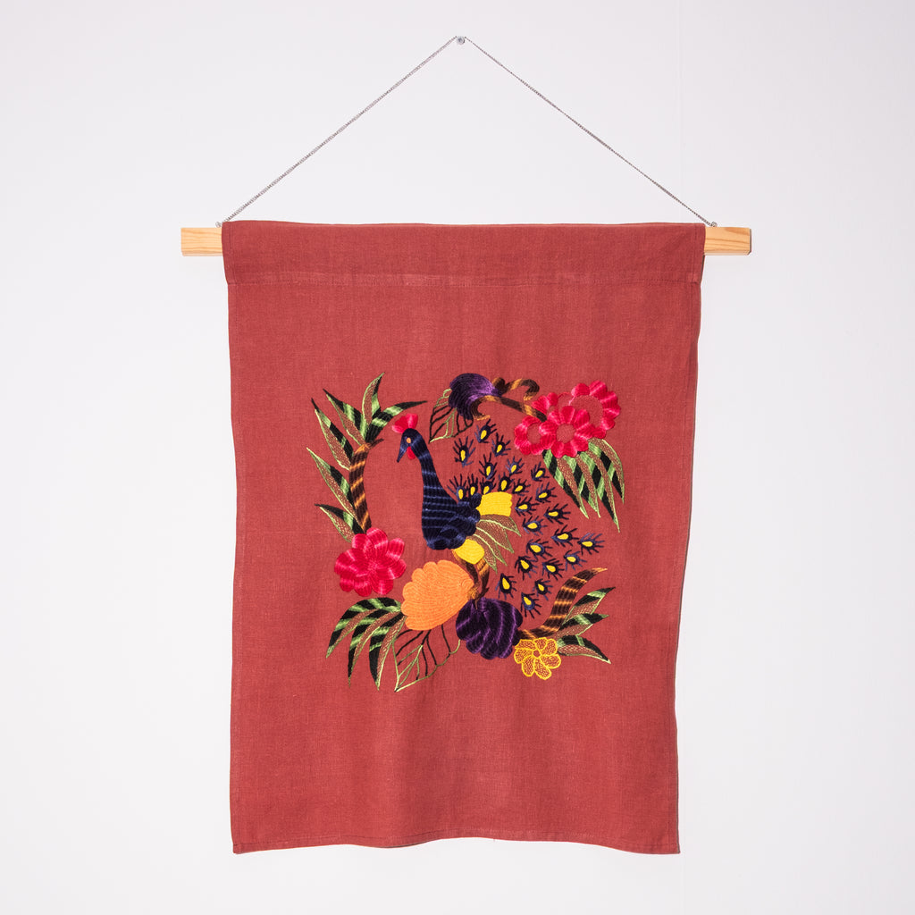 Peacock wall hanging on red linen